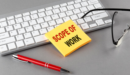 SCOPE OF WORK text on a sticky with keyboard, pen glasses on grey background