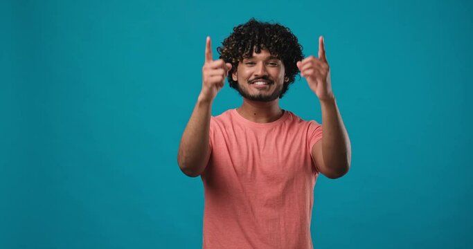 young indian man pointing index finger on camera standing isolated over blue studio background
