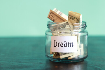 Save money for a dream. Glass jar with dollars on a wooden table. Piggy bank with banknotes for a dream close-up. Copy space