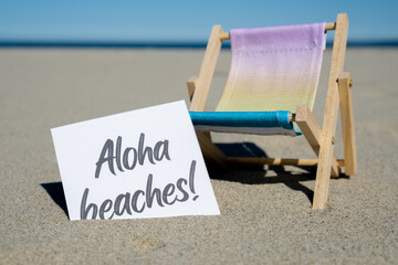 ALOHA BEACHES text on paper greeting card on background of beach chair lounge summer vacation...