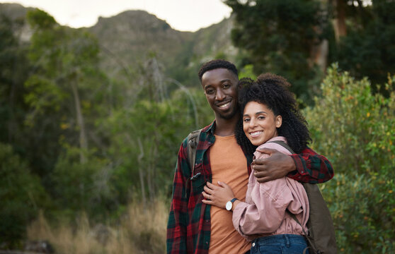Smiling young multiethnic couple standing arm in arm on a hiking trail