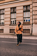 A hijab woman, donning a luxurious vintage French outfit, as she walks through the city streets at sunset, carrying bread, a bouquet of flowers, and newspapers in her hand, evoking a captivating blend