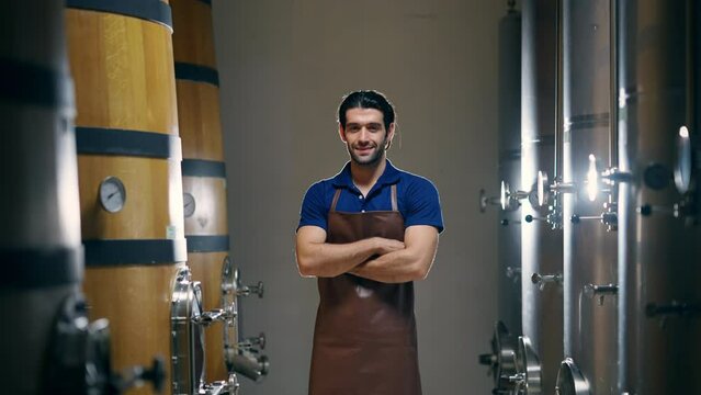 Portrait of Professional Caucasian man winemaker standing in modern wine cellar with stainless steel barrels with arm crossed. Winery manufacturing, Alcohol and wine winemaking quality control concept