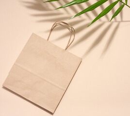 Empty disposable brown kraft paper bag with handles on beige background, eco packaging, zero waste