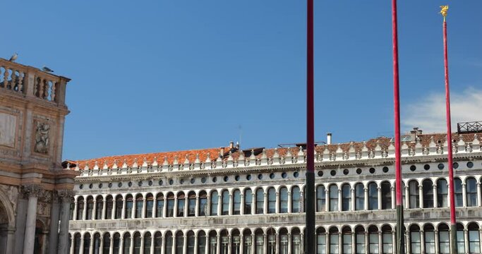 View from Piazza San Marco (St Mark's Square) to The Loggetta at the foot of the Campanile, Procuratie Vecchie, clocktower and St Mark's Basilica against a bright blue sky on a sunny day in Venice.