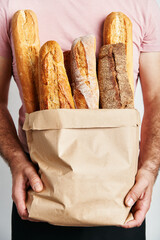 Man holds fresh loaves of bread baguettes in paper bag over light background