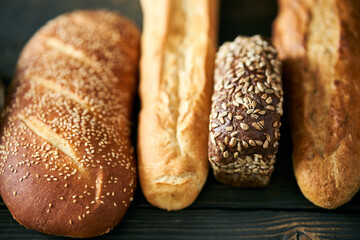 Different types of bread loaves on dark wooden background