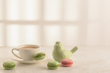 Coffee, macaroons and a porcelain figurine of a bird on a white table. Cozy breakfast.