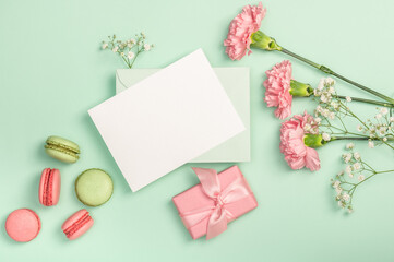 Flat lay composition with empty blank, gypsophila, pink carnations and macaroons on a light green...