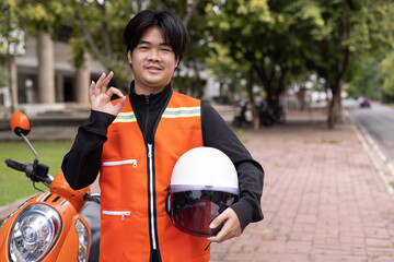 Happy young Thai motorcycle taxi driver or rider waiting for passenger near by the building in the city.