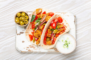 Traditional Greek Dish Gyros: Pita bread Wraps with vegetables, meat, herbs, olives on rustic wooden cutting board with Tzatziki sauce, olive oil top view, white wooden summer background.