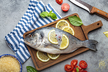 Raw fish dorado with ingredients lemon, fresh basil, cut cherry tomatoes, uncooked rice on wooden...