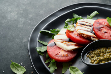 Caprese salad. Italian caprese salad with sliced tomatoes, mozzarella cheese, arugula, basil, olive oil in black plate over old brick tiles black background. Delicious Italian food. Top view.