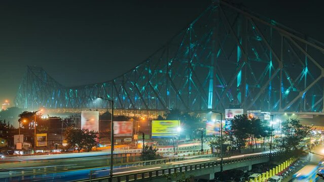 Timelapse view of traffic exiting architectural landmark Howrah Bridge illuminated at night in Kolkata, West Bengal, India, zoom out. 
