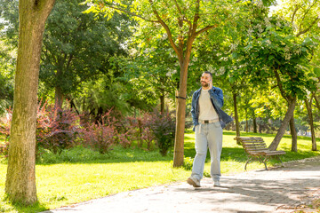 Young bearded man talking on the phone, enjoying a sunny day in a natural park.