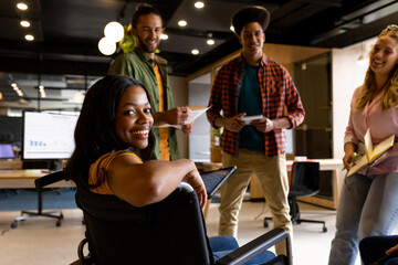 Happy african american woman in wheelchair with diverse colleagues at casual office meeting