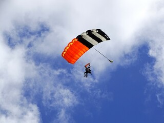 Skydiver gliding down with blue sky and clouds in the background
