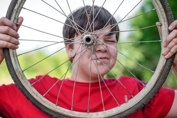 A carefree, cheerful and happy boy looks through the wheel of a retro bicycle in nature in summer.