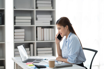 Charming Asian businesswoman focusing on her work, using her smartphone to contact with her clients.