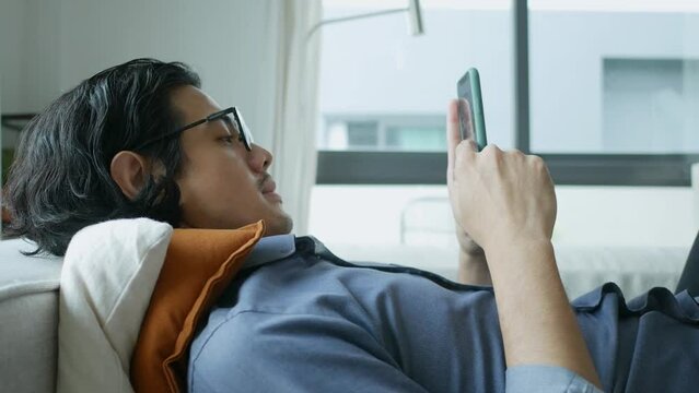 A man finds solace on a comfortable sofa in his living room. This relatable scene blends relaxation with digital connection, perfect for lifestyle, technology, and social media themes