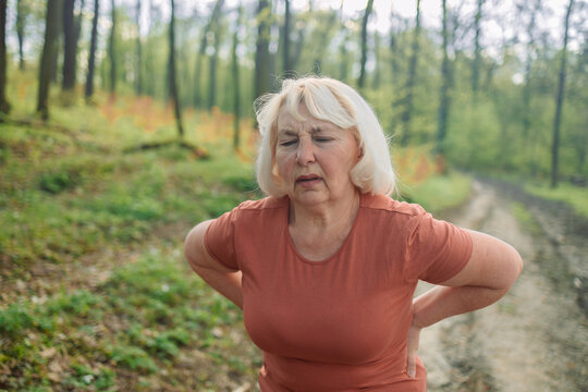 Tired senior 50s 60s athlete runner exhausted of cardio workout breathing hard after difficult exercise in a park. Caucasian fitness woman running s muscle back pain or cramps. High quality photo