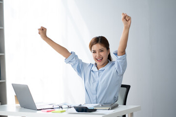 Cheerful young Asian business woman feeling overjoyed and celebrating after hearing the good news from her boss.