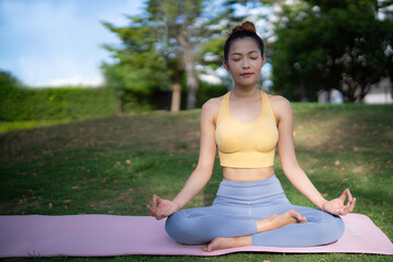 An  asian woman in yellow sport bra and gray lagging do meditating with peaceful emotion at park, healing, main tain health and mind and release stress concept.