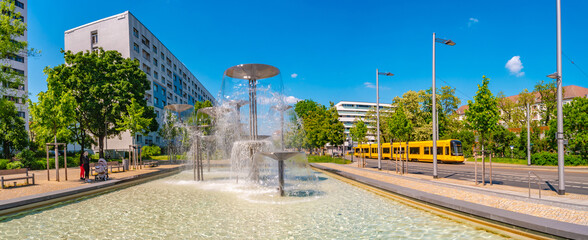 Dresden, Germany - Panoramic over fountain called Schalenbrunnen in Dresden with famous yellow tram. Cityscape of the downtown at sunny Spring day and blue sky. - obrazy, fototapety, plakaty