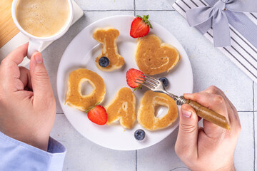 Father's day holiday idea for a cute surprise gift. Child preparing breakfast for dad, creatively decorated pancakes with the inscription I love Dad. Top view copy space, blue background