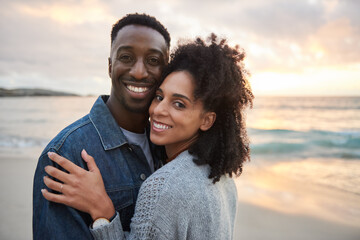 Smiling multiethnic couple standing arm in arm on a beach at sunset