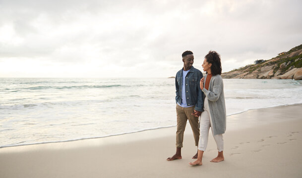 Smiling young multiethnic couple holding hands while walking on a sandy beach