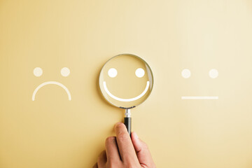 Hand holding magnifier happy smiley face icon among emotions. Good feedback rating, customer review, and satisfaction survey. Experience, mental health concept. Certificate signifies satisfaction.