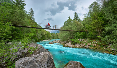 woman crossing  River Soca with her electric mountain bike over a suspension bridge in the Triglav...