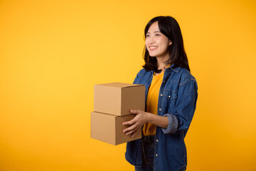 Portrait asian young woman wearing yellow t-shirt and denim shirt holding parcel box isolated on yellow studio background, Delivery courier and shipping service concept.