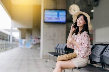 young asian woman traveler with weaving basket using a mobile phone and waiting for train in train station. Journey trip lifestyle, world travel explorer or Asia summer tourism concept.