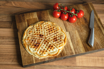Pizza waffle with pepperoni, olives and parmesan cheese and cherry tomatoes on a cutting board on the kitchen table