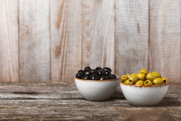 Green and black olives on a brown wooden background. Various types of olives in bowls and olive oil with fresh olive leaves. Copy space. Place for text. Mediterranean food. Vegan.