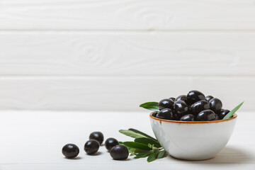 Black olives on a white wooden background. Various types of olives in bowls and olive oil with fresh olive leaves. Copy space. Place for text. Mediterranean food. Vegan.