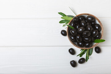 Black olives on a white wooden background. Various types of olives in bowls and olive oil with fresh olive leaves. Copy space. Place for text. Mediterranean food. Vegan.