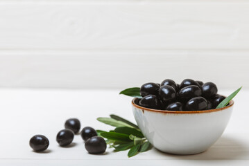 Black olives on a white wooden background. Various types of olives in bowls and olive oil with fresh olive leaves. Copy space. Place for text. Mediterranean food. Vegan.