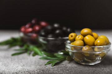 Green, black and red olives on a textured marble background. Various types of olives in bowls and olive oil with fresh olive leaves. Copy space. Place for text. Mediterranean food. Vegan.