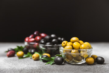 Green, black and red olives on a textured marble background. Various types of olives in bowls and olive oil with fresh olive leaves. Copy space. Place for text. Mediterranean food. Vegan.