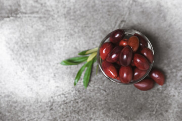 Red olives on a marble background. Various types of olives in bowls and olive oil with fresh olive leaves. Copy space. Place for text. Mediterranean food. Vegan.