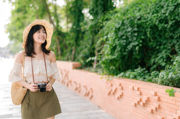 Portrait of asian young woman traveler with weaving hat and basket and a camera on green public park nature background. Journey trip lifestyle, world travel explorer or Asia summer tourism concept.