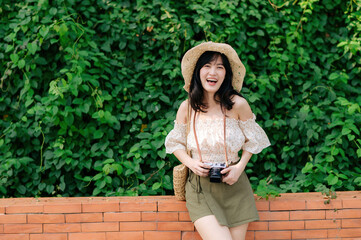 Obraz premium Portrait of asian young woman traveler with weaving hat and basket and a camera on green public park nature background. Journey trip lifestyle, world travel explorer or Asia summer tourism concept.