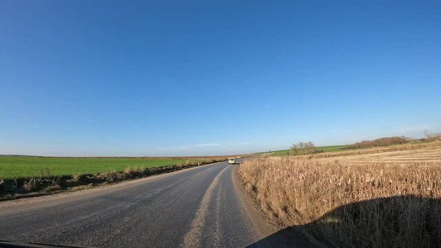 4K footage from moving vehicle on road in daylight. Fields and rural scenery on either side of road. POV driving stock video. 