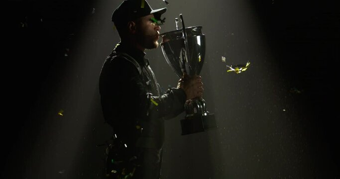 Silhouette of race car driver celebrating the win in a race against bright stadium lights, rising a trophy over his head