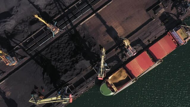 Top view from drone of a sea port. Black coal piles with cranes and tanker.