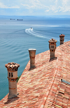 View of the Trieste Gulf from the Duino Castle with a powerboat leaving a wake among the waves; tiles roof and chimneys in foreground.