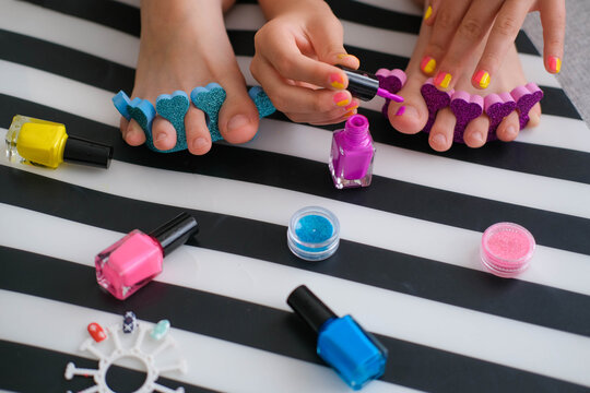 Children's feet with bright pedicure and manicure of different colors and bottles of bright nail polish. Little girl does a pedicure. Beauty salon game. Children's entertainment.